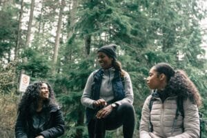 Three women enjoying a relaxing break during a forest hike, smiling and chatting.