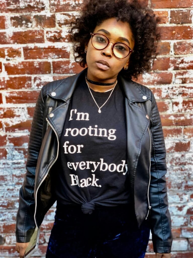 pexels-photo-938013-938013 Confident Black woman in a leather jacket and statement tee against a brick wall.