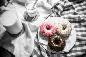 Three vibrant donuts with milk on a checkered cloth, creating a delightful food scene.