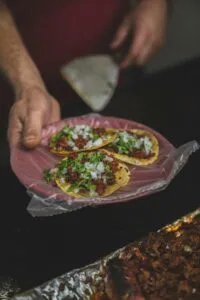 Close-up of three authentic Mexican street tacos with garnishes served on a plate.